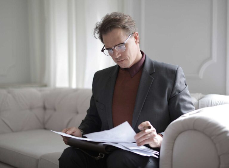A man sitting on top of a couch looking at papers.