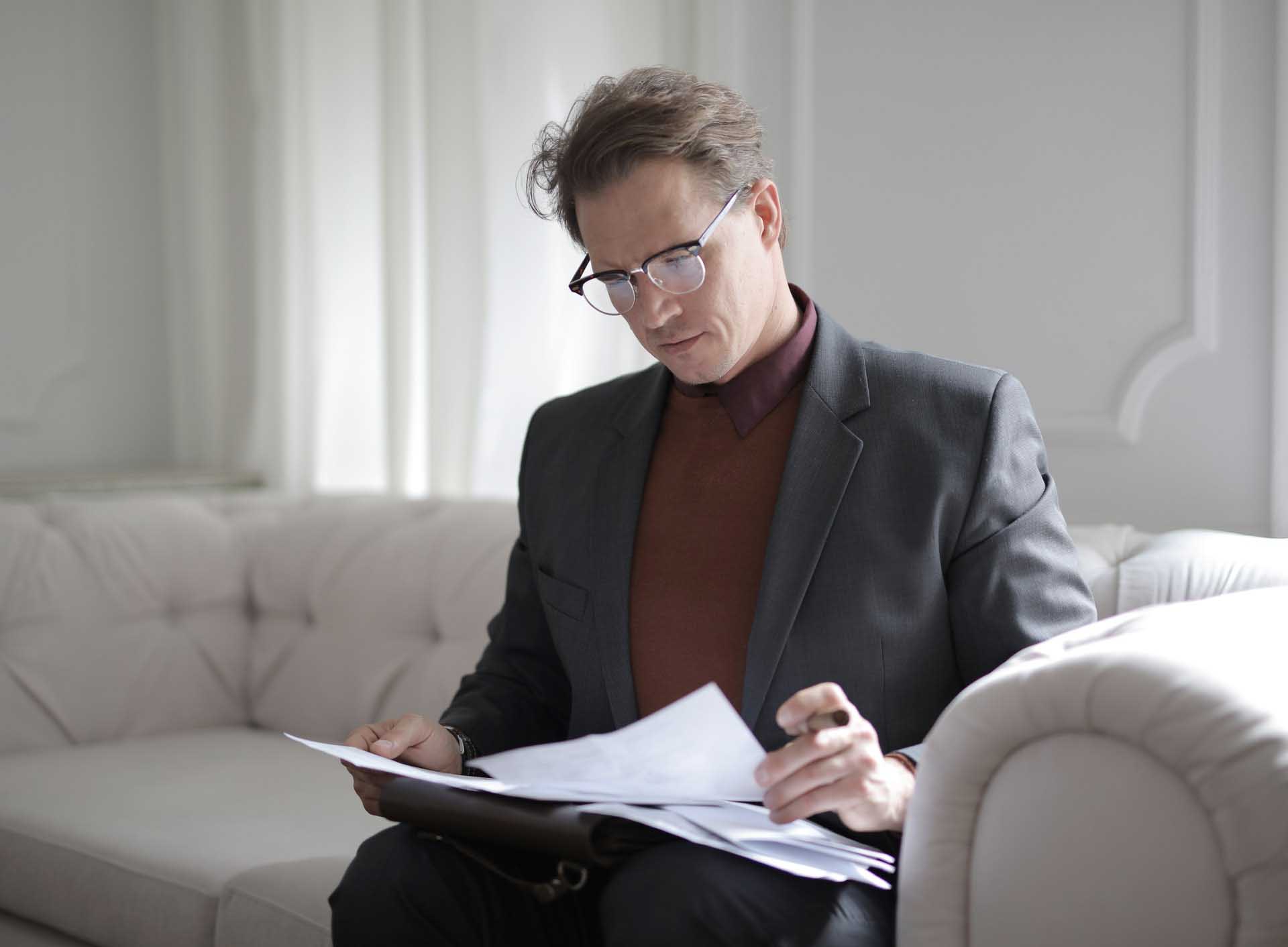 A man sitting on top of a couch looking at papers.