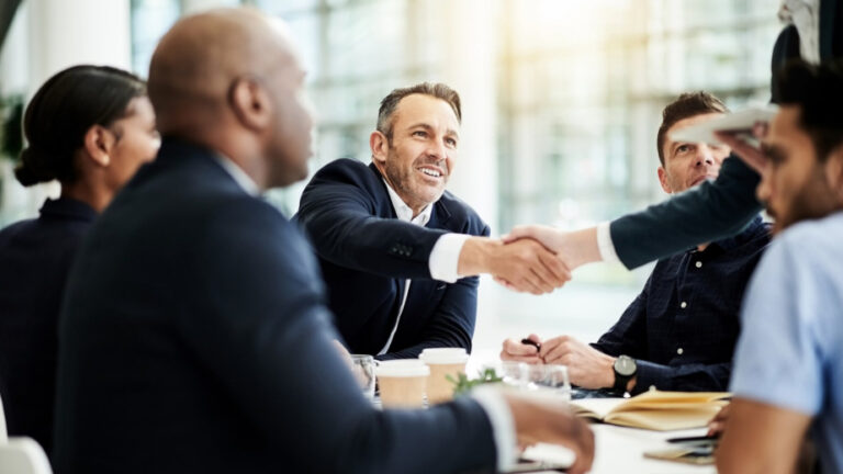 A group of people sitting at a table shaking hands.